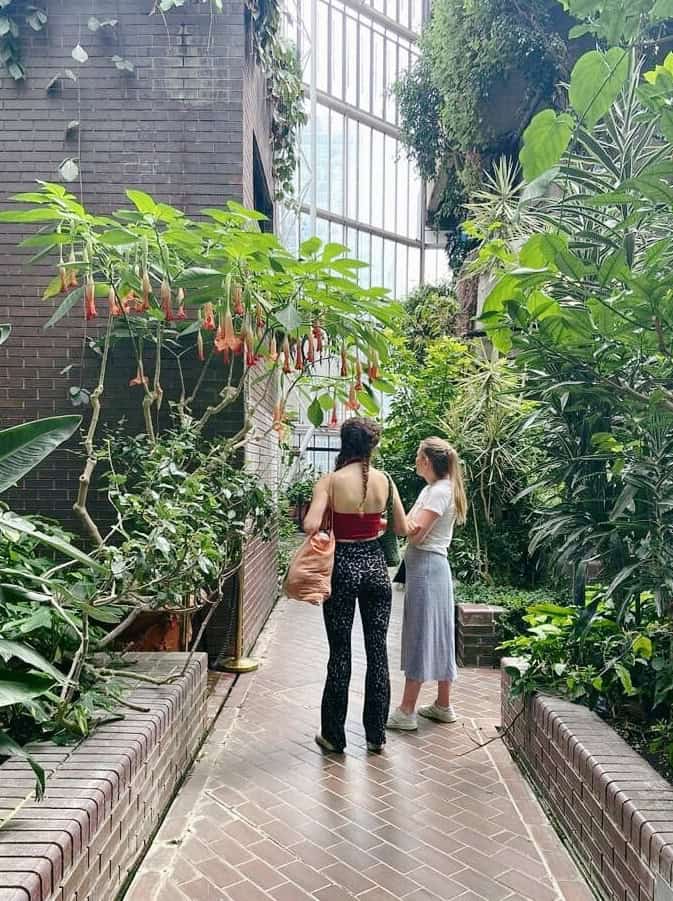 Jenny, owner of London Localite stood next to her friend in the Barbican Conservatory looking up at orange flowers