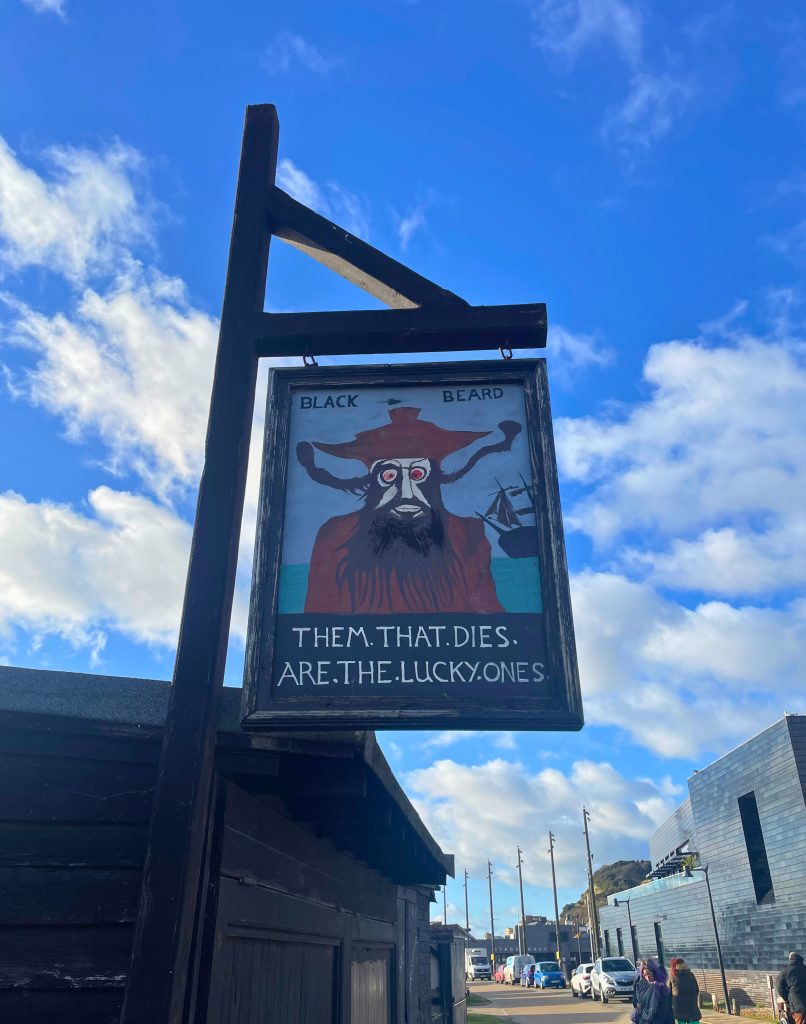 Quirky pirate sign in Hastings that reads 'them that dies are the lucky ones'